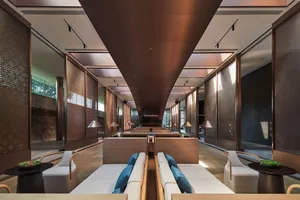 A contemporary hotel lounge area with wooden furniture, concrete flooring, and decorative room dividers.