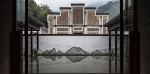 A modern lobby with concrete flooring and walls, featuring a water feature with rocks and a traditional Chinese architectural