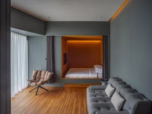 A modern minimalist bedroom featuring wooden furniture, a gray sofa, and an orange accent area with a built-in bed.