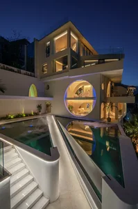 An elegant, modern residential home featuring glass walls, concrete terraces, and a steel framework.