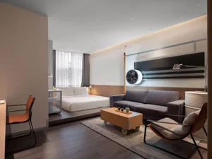 A minimalist hotel suite featuring a wooden floor, a gray fabric couch, and a metal table.
