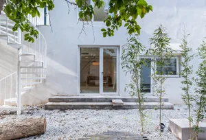 A modern residential exterior with concrete steps, gravel ground cover, and a spiral staircase.