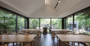 A spacious modern restaurant interior features large windows with a view of greenery, wooden tables, and glass railings.
