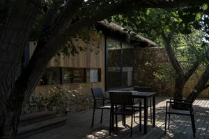 Outdoor patio area with wooden furniture, rock wall, and greenery.