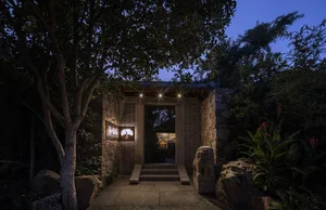 A classical entrance with brickstone walls and a garden featuring greenery and rocks.