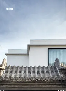Modern building with white walls and concrete roof tiles against a cloudy sky.