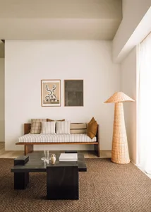 A modern living room featuring a wooden sofa, woven-fiber floor lamp, and abstract wall art.
