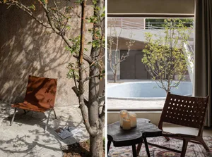 A metal chair and a small table with three candles in a space with a concrete wall and a tree casting shadows on it.