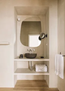 A minimalist bathroom with a concrete sink, wall-mounted faucet, and a round mirror above it. The space is adorned with white