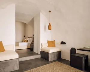 A minimalist bedroom with beige and orange cushions on a concrete bench, and a woven pendant light.