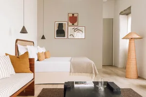 A minimalist bedroom with neutral tones, featuring a bed, modern pendant lights, abstract art, and a rattan floor lamp.