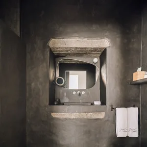 A minimalist bathroom with a concrete wall and sink, featuring a mirror and minimalist design elements.