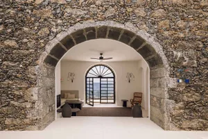 A minimalist interior entryway with stone walls, an arched doorway, and ocean view.