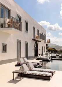 Modern minimalist hotel pool deck featuring concrete flooring, daybeds with striped cushions, and a serene outdoor space.