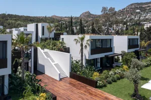 Modern residential house with white walls, glass windows, concrete stairs, and lush greenery.