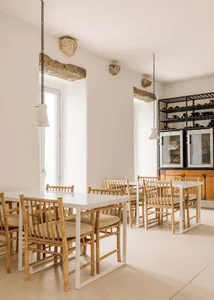 A minimalist restaurant dining room with white walls, wooden tables and chairs, and hanging stone decor.