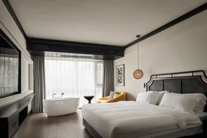 Modern minimalist bedroom with a white bed, yellow armchair, and white bathtub under a large window.