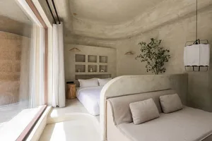 A minimalist bedroom with concrete walls, a large bed, and a grey sofa.