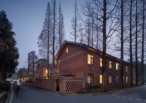 Residential building with red brick walls and illuminated windows, surrounded by tall trees in twilight.