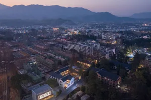 A modern cityscape at dusk with illuminated buildings and mountains in the background.