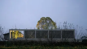 A modern concrete structure with a lattice facade, surrounded by trees and flowers.