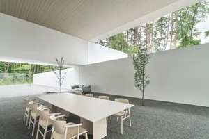 Modern, minimalist conference room with white walls and concrete floor, featuring a long white table and chairs.