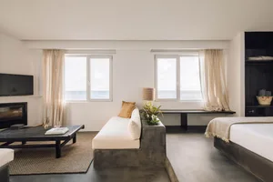 Modern hotel room featuring a concrete sofa, fabric cushions, and wooden elements, with a view of the ocean through large win