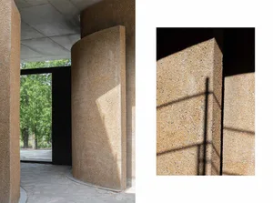 Modern interior space with concrete walls and structural columns, featuring sunlight casting shadows on the walls.