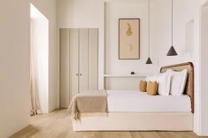 A modern minimalist bedroom featuring a bed with a wooden headboard, white bedding, and wooden flooring.