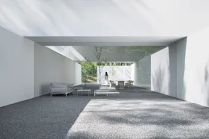 An enclosed minimalist living room with concrete flooring, white walls, and a white sofa.