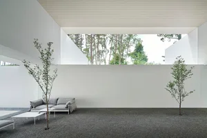Minimalist living space featuring modern furniture and gravel flooring surrounded by green plants and concrete structures.