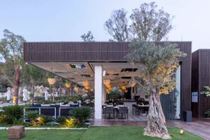 A modern outdoor restaurant with wooden panels, trees, and large windows overlooking a natural landscape.