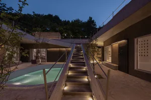 Concrete stairs leading up to a modern residential building at night, with a pool and trees in the background.