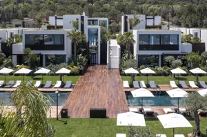 Modern exterior of a residential building featuring glass windows, wooden decks, and lush greenery.