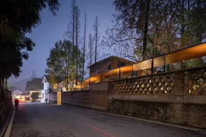A residential brick house illuminated at dusk with a long, wooden railing and trees in the background.