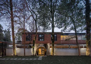 A modern house with brick and concrete exterior, surrounded by trees, at dusk.