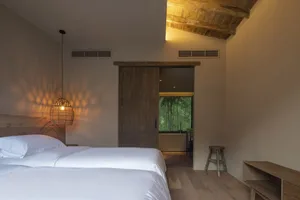 Bedroom with minimalist decor, featuring a wooden bed and a wicker pendant lamp.