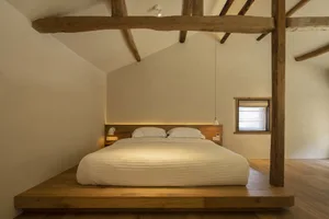 A minimalist bedroom featuring a wooden platform bed with white bedding and a window