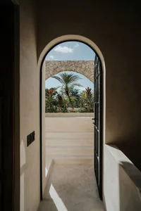 Minimalist architectural corridor with concrete floor and walls, featuring an arched doorway leading to a tropical garden.