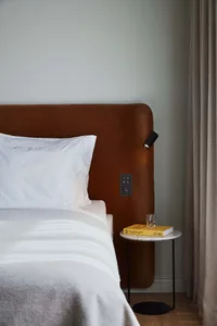 A minimalist bedroom with a brown upholstered headboard, white bedding, and a small marble side table.