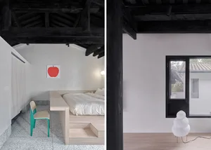 A minimalist bedroom with a wooden bed platform, black beamed ceiling, and a red apple poster.