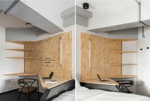 A minimalist bedroom features a wooden workstation with shelves and a laptop.