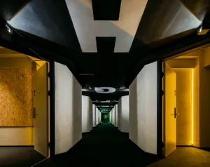 A minimalist corridor with concrete and white walls, featuring closed white doors and yellow lights on the right side.