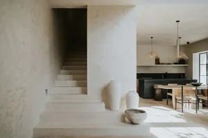 A minimalist kitchen with concrete elements, featuring a dining table and pendant lights.