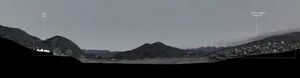 A panoramic view of a landscape featuring mountains, a village, and a site with a white building.