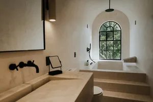 Modern bathroom with concrete finishes, a large arched window, and a freestanding bathtub.
