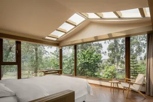 A modern bedroom featuring a white bed, large windows, wooden flooring, and a skylight.
