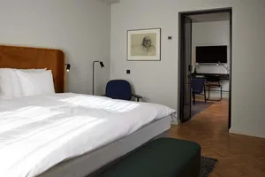 A modern bedroom with a bed, two chairs, and a desk with a computer.