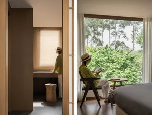 A modern bedroom featuring wooden furniture and large windows overlooking greenery.