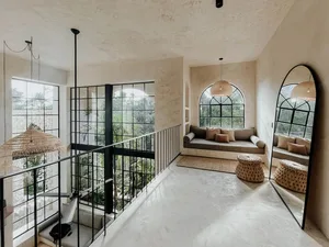 A modern living room with concrete walls, arched windows, and rattan furniture.